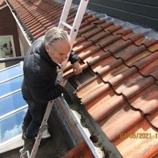Inspector on a ladder checking the tiles and gutter beside a rooflight