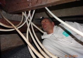 Inspector in a crawl space between plastic pipes and cables, checking under the floor of an Amsterdam flat