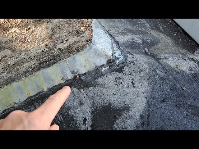 Vinger wijst naar een gescheurde naad in de bitumen dakbedekking