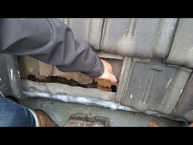 Hand pointing into a gap under lifted roof tiles above a zinc gutter