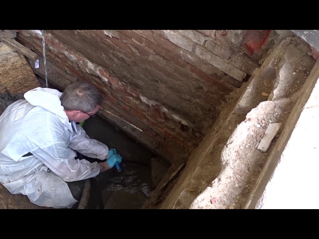 Inspecteur in witte overall in een inspectieput langs de gevel
