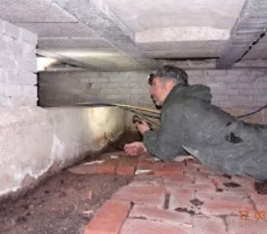 Inspector lying in a low brick crawl space under the floor joists during a damp survey